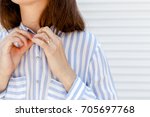 Stylish woman wearing blue striped shirt buttoning a button. Details of trendy casual outfit. Street fashion. Gold rings on female fingers. Jewelry, accessories, close up, women hands.