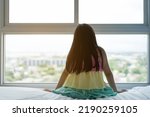 Small photo of back asian children or kid girl sitting alone on white bed and lonely depressed or suppressed young woman and sad child in bedroom at home with morning warm sunlight on window and wake up late in city