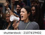Small photo of Young caucasian woman protester demonstrate shouting loud through megaphone while being on a protest - multicultural men and women protestors on a global strike demonstration