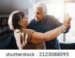 Small photo of Retired active couple dancing in the living room - Pair of sprightly grandparents dancing and having fun in the living room