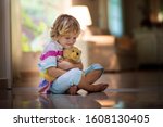 Child playing with teddy bear. Little boy hugging his favorite toy. Kid and stuffed animal at home. Toddler sitting on the floor of living room with big window at sun set. Kids play indoors.