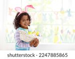 Small photo of Kids dyeing Easter eggs. Children in bunny ears dye colorful egg for Easter hunt. Home decoration with flowers, basket and rabbit for spring holiday celebration. Little curly boy decorating home.