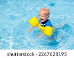 Small photo of Baby with inflatable armbands in swimming pool. Little boy learning to swim in outdoor pool of tropical resort. Swimming with kids. Healthy sport activity for children. Sun protection. Swim aids.