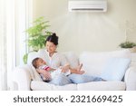 Small photo of Mother and baby under cool air conditioner. Comfortable temperature at family home. Cooling and heating device. Asian mom and kid on couch under cold breeze. Air conditioning on hot summer day.
