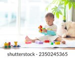 Small photo of Adorable Asian baby boy learning to crawl and playing with colorful block toy in white sunny bedroom. Cute laughing child crawling on a play mat. Nursery, clothing and toys for little kids.