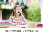 Small photo of Child doing homework for school at white desk. Little girl with school supplies, abc books, drawing and painting tools and materials. Happy back to school student. Kid learning alphabet letters.