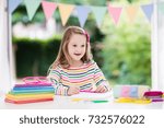 Small photo of Child doing homework for school at white desk. Little girl with school supplies, abc books, drawing and painting tools and materials. Happy back to school student. Kid learning alphabet letters.