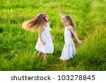 Two adorable girl in white dresses dancing on the meadow