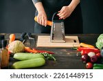 Woman cooking in kitchen at home. Cropped image of female hands rubs carrots on a grater. Culinary, healthy eating concept
