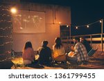 Group of young friends watching a movie on a building rooftop terrace, eating popcorn, drinking beer and having fun