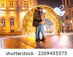 Couple in love hugging on city square with Christmas lights all around, spending time outdoors in the nicely decorated city streets during winter holiday season and advent