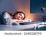 Tired woman sleeping at her desk while working late in an office; woman leaning on her desk and taking a power nap while working overtime