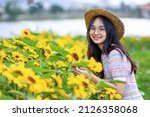 portrait of young asian woman in beautiful casual clothes with straw hat in full bloom sunflower fields on sunny day. Happy woman smiling in sunflower field