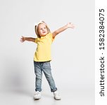 Small photo of Kid baby girl blonde in yellow t-shirt is playing popstar talent show singing dancing with her hands up spread showing how big it was on white background