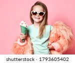 Happy smiling stylish rich kid girl in faux fur coat and sunglasses holds big tasty ice cream with candies in waffles cone on pastel pink background