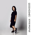 Small photo of Portrait in profile of self-reliant asian kid girl in black long t-shirt dress and bob hairstyle showing off demonstrating her new black sandals shoes and looking down at camera