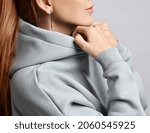 Small photo of Portrait in profile of young slim red-haired woman with perfect healthy straight long hair and skin wearing trendy clothing grey hoodie holding her cowl with hands. Side view