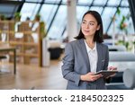 Young Asian business woman entrepreneur standing in office holding digital tablet. Businesswoman leader, professional company manager using smart corporate management technology looking at copy