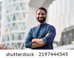 Small photo of Happy confident wealthy young indian business man leader, successful eastern professional businessman crossing arms looking at camera posing outdoors in urban big city for close up headshot portrait.