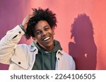 Small photo of Close up portrait photo of young happy African American cool hipster teen guy face laughing on red city wall lit with sunlight. Smiling cool rebel gen z teenager model standing outdoors. Headshot.