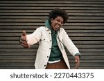 Small photo of Happy funky funny generation z hipster rapper African American guy dancing, singing, having fun feeling hip-hop or rap vibe, moving and gesturing standing at wooden wall outdoors.
