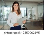 Small photo of Happy 45 years old Latin professional middle aged business woman corporate leader, happy mature female executive, lady manager standing in office holding clipboard looking at camera, portrait.