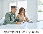 Small photo of Happy middle aged mature man and woman paying bills online at home. Older senior couple using laptop computer checking insurance or financial invoice counting taxes sitting at table in living room.