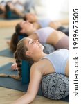 Small photo of Restorative yoga with a bolster. Group of three young sporty attractive women in yoga studio, lying on bolster cushion, stretching and relaxing during restorative yoga. Healthy active lifestyle