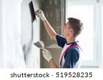 Thirty years old manual worker with wall plastering tools renovating house. Plasterer renovating indoor walls and ceilings with float and plaster.