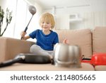 Small photo of Mischievous preschooler boy play the music using kitchen tools and utensils at home during lockdown. Funny drum part from child. Entertainment a little kids at home.