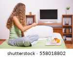 Young woman sitting in her bed and watching TV. It's time for breakfast.