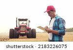 Small photo of Agriculture. farmer working on a digital tablet in a field in the background tractor plows ground in a field of wheat. farming agriculture concept. business farmer in the field