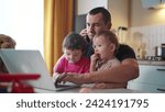 Small photo of father working from home remotely with two baby in his arms. pandemic remote work business concept. father tries to work at fun home in kitchen, baby children interfere sitting on their hands
