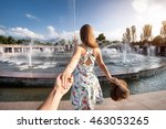 Woman in white dress with hat holding man by hand and going to fountain in the park in Almaty, Kazakhstan