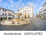 Small photo of Low-angle shot of a fountain surrounded by traditional residential building and with Saint Anton's Church in the background, Giraldo Square, Evora, Alentejo, Portugal
