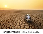 Climate change Young man paddle a boat at dry cracked earth with orange sky and hot weather of the sun. Metaphor Global warming, Drought and water crisis concept.