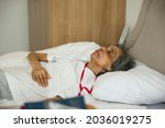 Small photo of Frail old Indian Asian woman lying in bed in a hospital room or nursing home, UK.