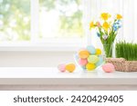 Easter eggs and spring flowers on white table over blurry kitchen window background