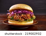 Pulled pork burger with red cabbage salad and bbq sauce on plate with dark background 