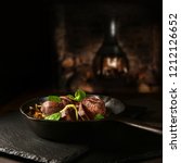 Small photo of Wild venison fillets roasted with garlic mushrooms, scallions and watercress salad in a wrought iron black skillet shot against a rustic wood burner background with copy space.