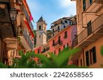 Traditional colorful houses on a street in old town with a view of the bell tower of Chiesa di San Lorenzo, Manarola in Cinque Terre, Italy