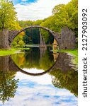 Small photo of Picturesque narrow bridge in the park Kromlau, Germany. The Devil's Bridge on the Rakots River. The basalt columns of the bridge form a perfect circle with their reflection in the water.