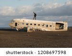 Old crashed plane in Iceland with traveler posing on the top