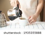 Crop of woman hand pouring finished slow coffee into white cup on table at home