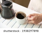 High angle of hand holding cup of coffee and jug on striped placemat at home