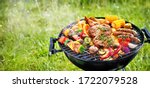 Assorted delicious grilled meat with vegetables on barbecue grill with smoke and flames in green grass