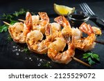 Grilled shrimp skewers served with soy sauce, garlic, fresh parsley and lemon on black plate