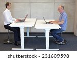 two men  coworking in correct sitting posture on pneumatic leaning seats  with laptops  at electric height adjustable desks in office