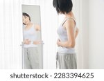 Small photo of Asian woman struggling with her diet in front of a mirror