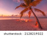 Romantic dinner on the beach with sunset, candles with palm leaves and sunset sky and sea. Amazing view, honeymoon or anniversary dinner landscape. Exotic island evening horizon, romance for a couple